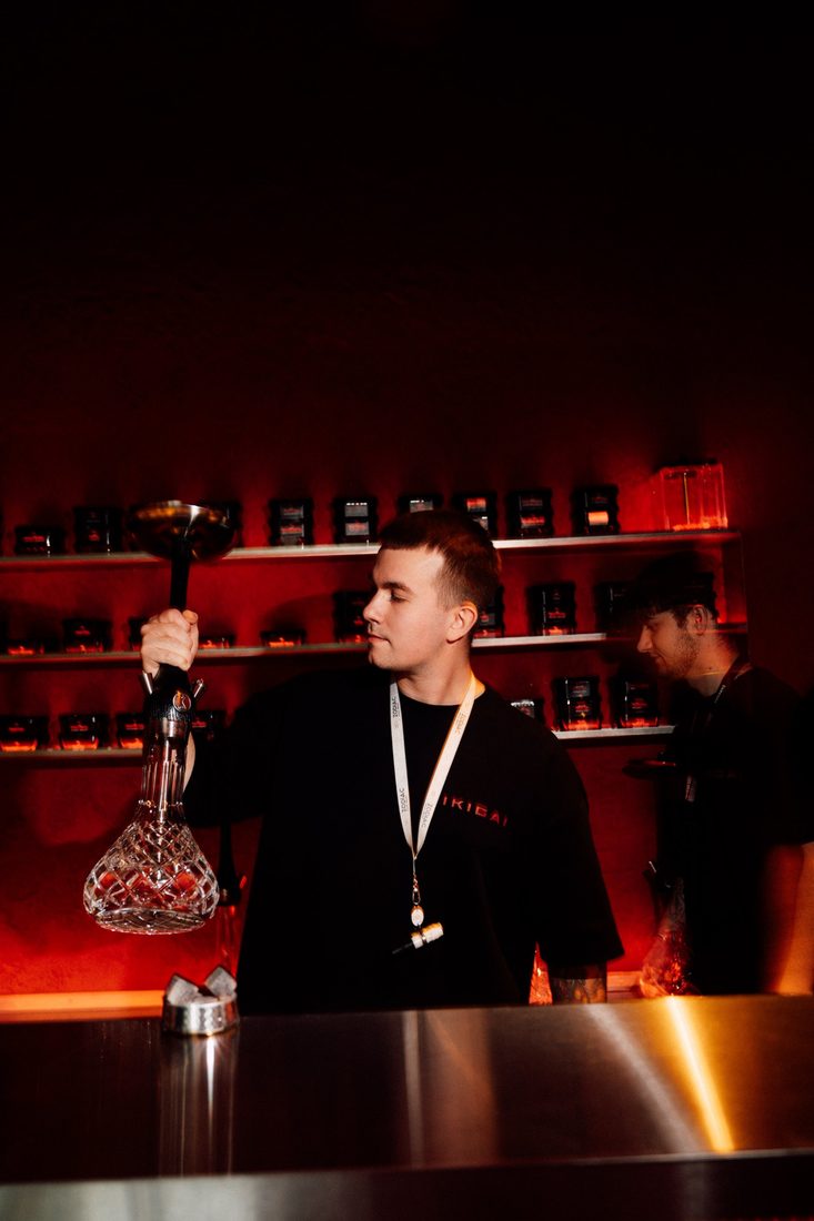 Hookah master lifting a crystal hookah in front of the red-lit shelf