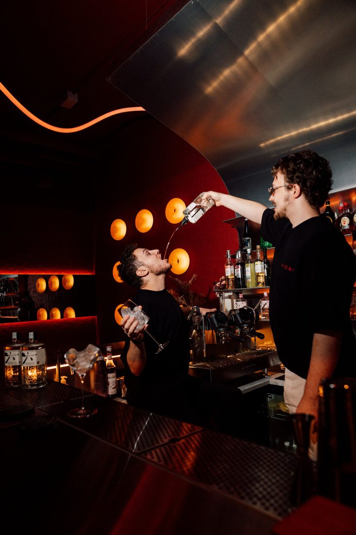 Bartender pouring a drink straight from the bottle in front of the lamp wall
